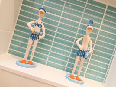 Two decorative duck figurines wearing blue swimwear and holding life rings on a white surface with teal tiled wall behind at Port View in Falmouth