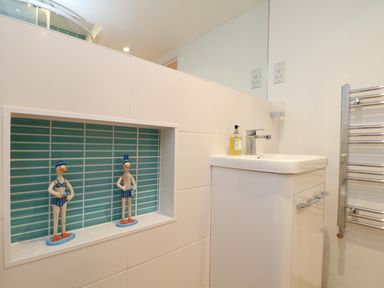 A bathroom sink with soap dispenser and two decorative duck figures in a wall niche with blue tiles at Port View in Falmouth