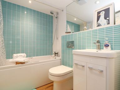 A bathroom with a bathtub shower toilet and sink with blue tile walls at Port View in Falmouth