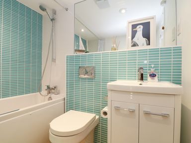 A bathroom with a bathtub shower toilet and sink with blue tiles at Port View in Falmouth