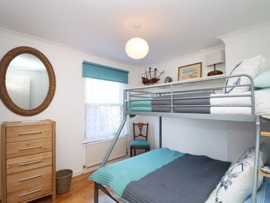 A bedroom with a bunk bed a wooden chest of drawers a round mirror and a chair at Port View in Falmouth