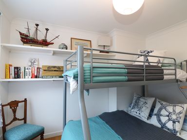 A bedroom with a bunk bed a wooden chair and shelves with books and a model ship at Port View in Falmouth