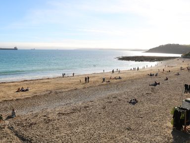 A sandy beach with people sitting and walking near the water and ships on the sea at Port View in Falmouth