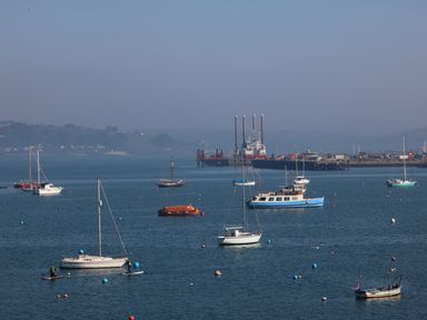 A harbor with various sailboats and motorboats on the water with a pier and industrial structures in the background at Port View in Falmouth