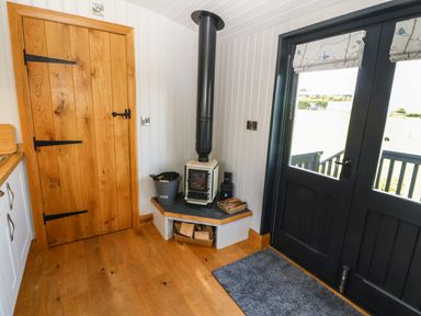 A corner of a room with a wood burning stove a wooden door and black double doors with glass panels at Cwt Y Rhos in Valley