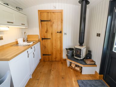 A kitchen corner with a wooden door a wood stove and white cabinets with a sink at Cwt Y Rhos in Valley