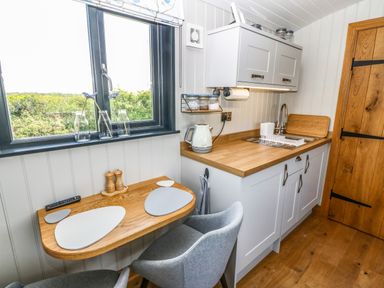A small kitchen with a wooden countertop a sink and a foldable wooden table with placemats and chairs at Cwt Y Rhos in Valley