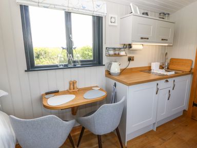 A small kitchen area with a wooden countertop sink and two grey chairs at a folding wooden table under a window with three glass vases at Cwt Y Rhos in Valley