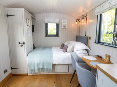 A bedroom with a double bed desk with two chairs and windows with floral blinds at Cwt Y Rhos in Valley