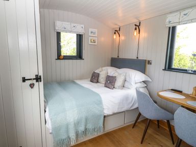A bedroom with a bed a small wooden table and two grey chairs at Cwt Y Rhos in Valley