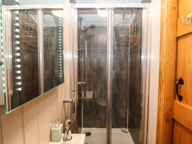 A bathroom shower area with glass doors a mounted showerhead a soap dish and a sink with a soap dispenser and towel at Cwt Y Rhos in Valley