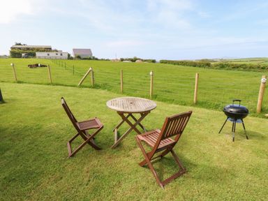 A garden with two wooden chairs around a round wooden table and a barbecue grill on grass at Cwt Y Rhos in Valley