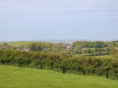 A rural landscape with green fields trees and houses in the distance at Cwt Y Rhos in Valley