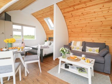 A small living area with a gray sofa and white coffee table next to a dining table and chairs with a bed in the background at Primrose in Seaton near Hornsea