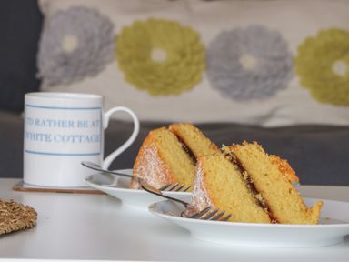 Two slices of sponge cake with jam on white plates and a white mug with blue text on a table at Primrose in Seaton near Hornsea