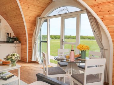 A dining area with a round table set with flowers and a bottle next to sliding glass doors in a wooden room at Primrose Seaton near Hornsea