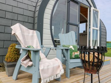 Two wooden chairs with cushions and a blanket on a wooden deck outside a pod at Primrose Seaton near Hornsea