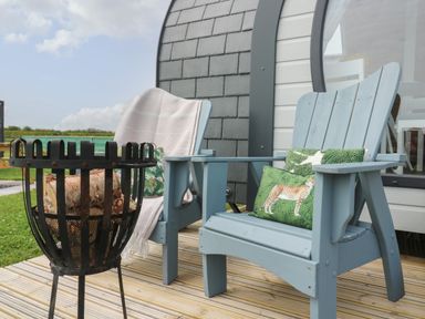 Two blue wooden chairs with cushions on a wooden deck next to a fire pit with logs Primrose Seaton near Hornsea