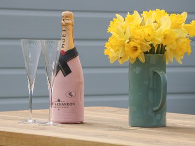 A bottle of Moet champagne with two clear champagne flutes and a green vase with yellow daffodils on a wooden table at Primrose in Seaton near Hornsea