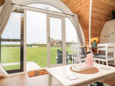 A dining area with a bottle of champagne on a table and large circular glass doors showing a grassy field at Poppy in Seaton near Hornsea