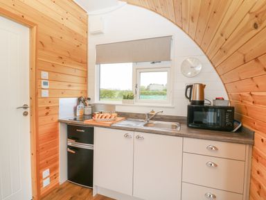 A small kitchen with wooden walls a sink a microwave a kettle a fridge and a window at Poppy in Seaton near Hornsea