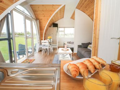A kitchen counter with croissants and juice looking into a living area with dining table couch and bed at Poppy in Seaton near Hornsea