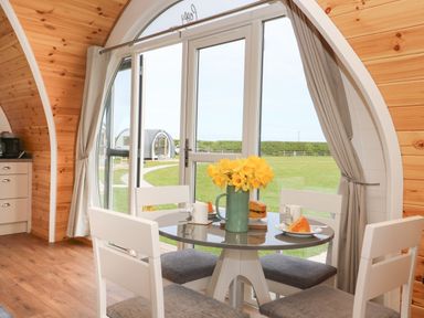 A dining area with a round table and four chairs next to large glass doors with curtains and a view of grassy outdoors at Poppy in Seaton near Hornsea