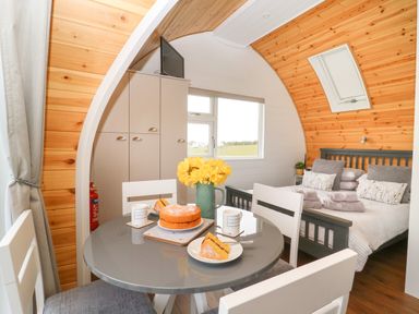 A dining table with cake and flowers next to a bed in a wooden cabin at Poppy Seaton near Hornsea