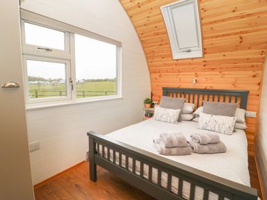 A bedroom with a double bed pillows towels wooden wall and window at Poppy in Seaton near Hornsea