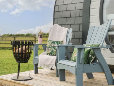 Two wooden chairs with cushions and a blanket on a wooden deck with a fire basket and a bottle of champagne at Poppy in Seaton near Hornsea