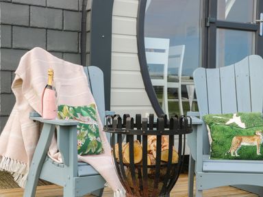 Two outdoor chairs with cushions and a basket of firewood on a wooden deck at Poppy in Seaton near Hornsea