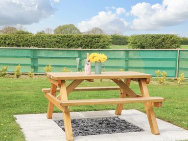 A wooden picnic table with a bottle of champagne flowers and two glasses on a patio in a garden at Poppy in Seaton near Hornsea