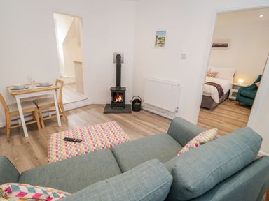 A living room with a wood-burning stove a dining table with chairs and a view into a bedroom at Ty Capel Bach in Rachub