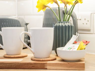 A kitchen counter with two white mugs on coasters a vase with yellow flowers and a bowl with tea bags at Ty Capel Bach in Rachub
