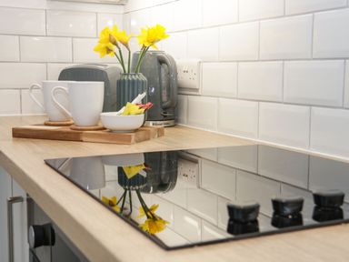 A kitchen countertop with an electric cooktop two mugs a vase with yellow flowers a kettle and a toaster at Ty Capel Bach in Rachub