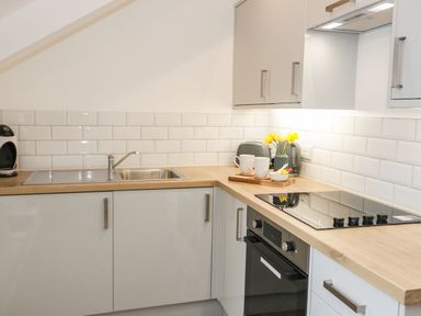 A kitchen with white cabinets a wooden countertop a sink a stovetop and a vase with yellow flowers at Ty Capel Bach in Rachub