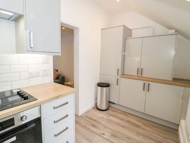 A kitchen with light wood countertops white cabinets a built in oven a stovetop and a stainless steel trash bin at Ty Capel Bach in Rachub