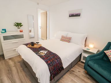 A bedroom with a double bed a white dresser a green armchair and a small bedside table at Ty Capel Bach in Rachub
