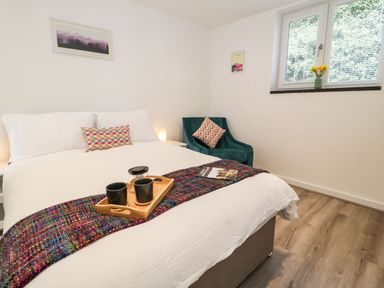 A bedroom with a bed a tray with mugs a navy chair and a window with flowers at Ty Capel Bach in Rachub
