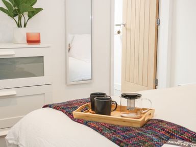 A bedroom with a white dresser and plant near a bed with a wooden tray holding black mugs and a glass teapot at Ty Capel Bach in Rachub