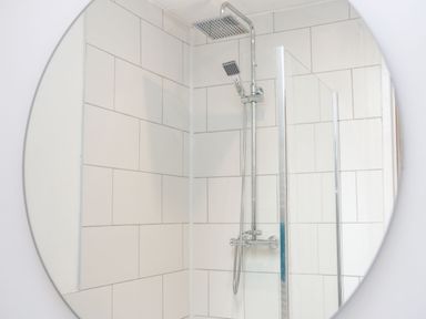 A shower area with white tiles and a dual showerhead visible in a round mirror at Ty Capel Bach in Rachub