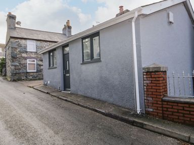 A narrow street with two houses one grey with a dark door and windows and one stone built with chimneys at Ty Capel Bach in Rachub