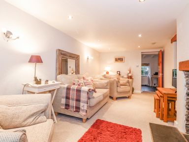 A living room with beige sofas a red rug a wooden mirror and lamp at Yanway Cottage in Troutbeck near Troutbeck Bridge