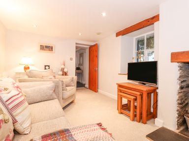 A living room with beige sofas a wooden tv stand with nested tables and a stone fireplace at Yanway Cottage in Troutbeck near Troutbeck Bridge
