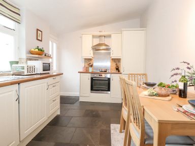 A kitchen with white cabinets a wooden dining table with chairs and food on it at Yanway Cottage in Troutbeck near Troutbeck Bridge