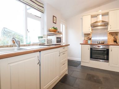 A kitchen with white cabinets wooden countertops a stainless steel oven and sink at Yanway Cottage in Troutbeck near Troutbeck Bridge