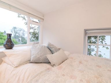 A bedroom with a bed and pillows near two windows with a vase on the window sill at Yanway Cottage in Troutbeck near Troutbeck Bridge