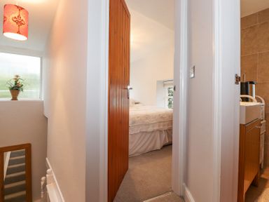 A hallway with a wooden door leading to a bedroom and a bathroom visible with a sink at Yanway Cottage in Troutbeck near Troutbeck Bridge