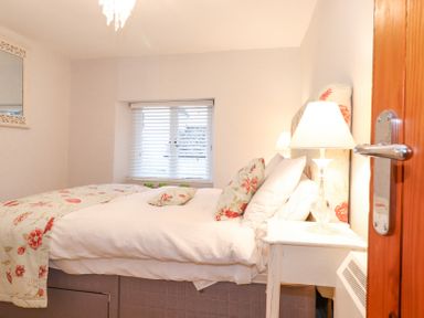 A bedroom with a bed with floral bedding and pillows a bedside table with a lamp and a window with blinds at Yanway Cottage Troutbeck near Troutbeck Bridge