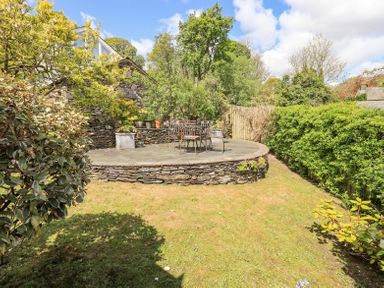 A garden with a circular stone patio holding metal chairs and table surrounded by hedges and trees at Yanway Cottage in Troutbeck near Troutbeck Bridge